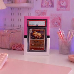 May include: A graded Pok&eacute;mon card in a pink and white holder. The card features an Arcanine illustration and text that reads "2023 POKEMON SV2a JP ARCANINE MASTER BALL REVERSE HOLD". The holder is displayed on a desk with other pink accessories.