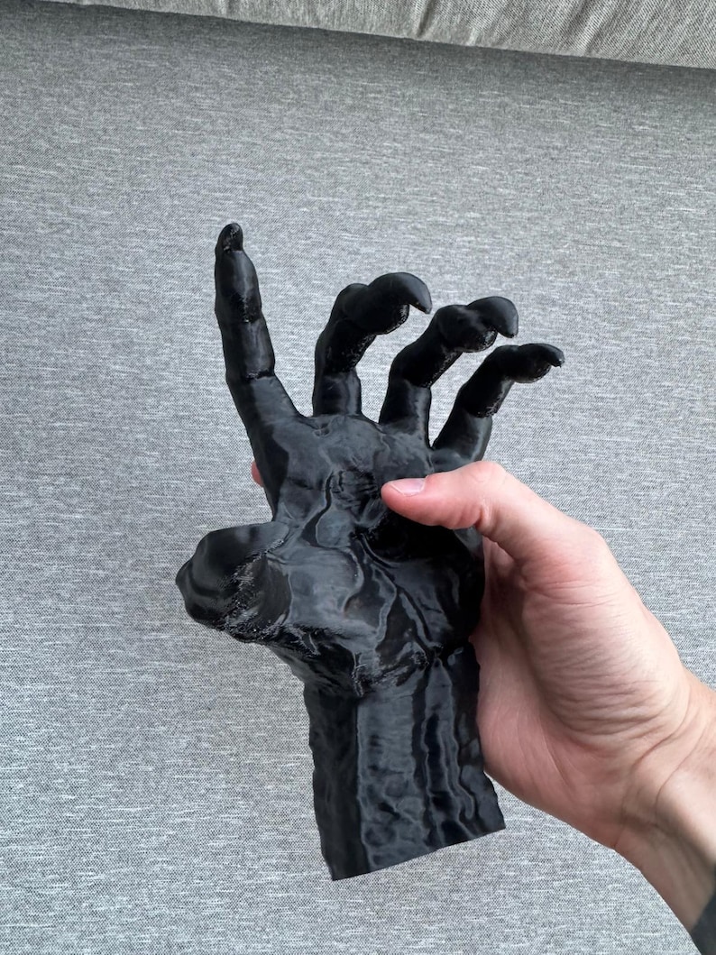 Puede incluir: Una escultura negra impresa en tres dimensiones de una mano con garras y dedos alargados y puntiagudos. La superficie tiene una apariencia texturizada y estratificada caracter&iacute;stica de la fabricaci&oacute;n aditiva, mostrando una forma oscura y r&iacute;gida.