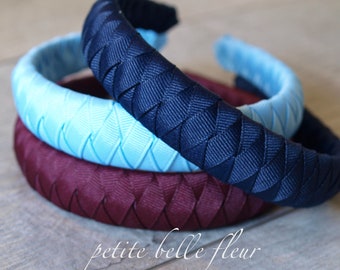 May include: Three braided fabric headbands in navy blue, light blue, and burgundy. The headbands are stacked on top of each other.