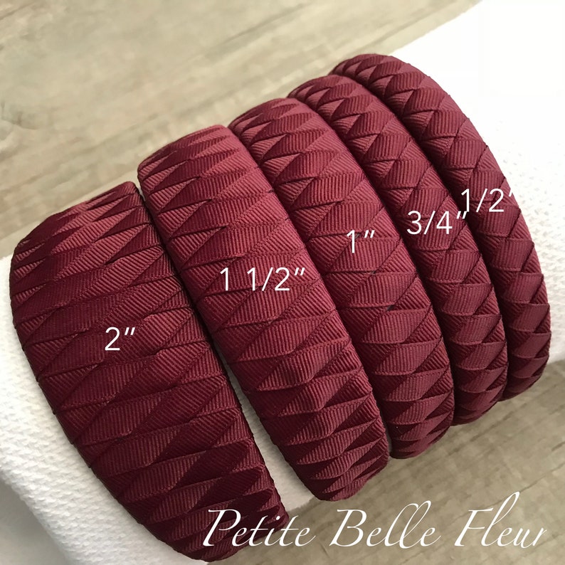 May include: A collection of burgundy headbands with a textured, geometric design. The headbands vary in width, labeled as 2", 1 1/2", 1", 3/4", and 1/2". The brand name "Petite Belle Fleur" is printed at the bottom.