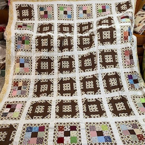 May include: A brown and white quilt with a repeating pattern of squares and circles. The squares are made of patchwork fabric in various colors and patterns. The circles are brown and have a geometric design.