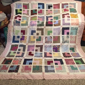 May include: A large quilt with a patchwork design featuring a variety of floral patterns in shades of pink, purple, blue, green, and brown. The quilt is made up of squares with a white background and a pink border.