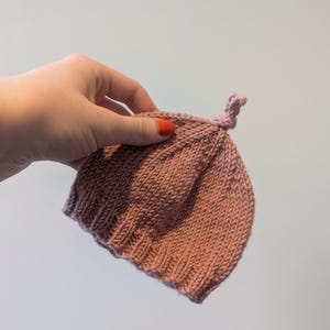 May include: A soft, pink knitted baby hat with a knotted top.