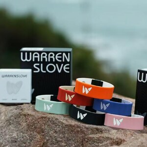Puede incluir: Una colección de pulseras coloridas con el texto "WARREN SLOVE" en el embalaje. Las pulseras son de varios colores, incluyendo naranja, rojo, azul, negro, rosa y verde, con un logotipo blanco. El fondo presenta una vista panorámica del océano.