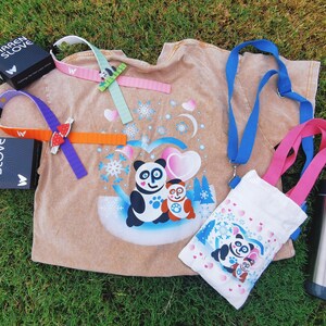 Puede incluir: Una colecci&oacute;n de art&iacute;culos con tem&aacute;tica de panda, que incluye una camiseta color canela con un gr&aacute;fico de panda, una bolsa tote blanca, un cord&oacute;n azul y una botella de agua de acero inoxidable. Tambi&eacute;n se incluyen varias pulseras coloridas y dos cajas negras con el texto "WARREN SLOVE".