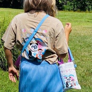 Puede incluir: Una camiseta color beige con un gr&aacute;fico de oso panda, falda plisada azul y gorra de b&eacute;isbol blanca con un dise&ntilde;o de panda. Un peque&ntilde;o bolso tote blanco con un gr&aacute;fico de oso panda se lleva al hombro con una correa azul.