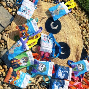 Puede incluir: Una colecci&oacute;n de peque&ntilde;as bolsas de mano coloridas con varios dise&ntilde;os de personajes de dibujos animados. Las bolsas tienen correas de diferentes colores, incluyendo azul, rosa, amarillo y naranja. Las bolsas est&aacute;n hechas de tela blanca con im&aacute;genes impresas de un panda, un conejo y otros personajes.