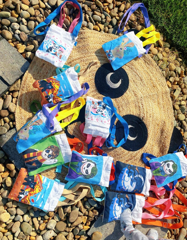 Puede incluir: Una colecci&oacute;n de peque&ntilde;as bolsas de mano coloridas con varios dise&ntilde;os de personajes de dibujos animados. Las bolsas tienen correas de diferentes colores, incluyendo azul, rosa, amarillo y naranja. Las bolsas est&aacute;n hechas de tela blanca con im&aacute;genes impresas de un panda, un conejo y otros personajes.