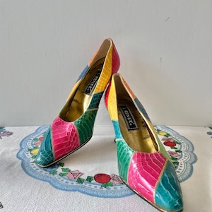 May include: A pair of colorful, patchwork-style high heels. The shoes feature a pointed toe and a stiletto heel. The color palette includes pink, green, yellow, and blue. The brand name "RENEE" is visible on the inner sole.
