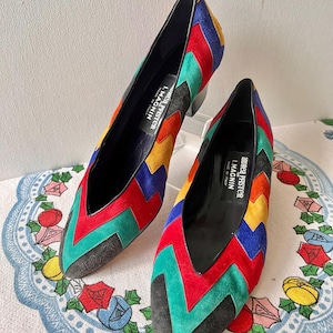 May include: A pair of vintage, colorful heels with a chevron pattern in red, green, yellow, blue, and black. The shoes have a pointed toe and a small heel. The brand name "Andrea Pfister L. Macnin" is visible inside the shoe.