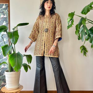 May include: A vintage gold and red patterned coat with a decorative clasp, paired with black flared pants and boots. The coat has three-quarter sleeves with blue trim. A fur hat completes the ensemble.