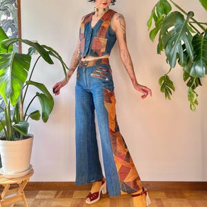May include: A denim vest and high-waisted flared jeans set with patchwork details in shades of brown, orange, and red. The outfit is paired with burgundy heels. The ensemble is a vintage-inspired fashion statement.