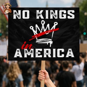 May include: A black sign held by a person in a crowd. The sign reads "NO KINGS in AMERICA" in white text, with a white crown crossed out in red. The background is a black flag with white stars.