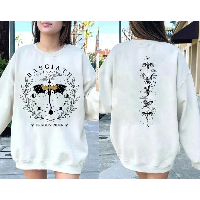 May include: Cream-colored sweatshirt with a graphic design on the front and back. The front features the text "BASGIATH WAR COLLEGE" in a circular design with a dragon and the words "DRAGON RIDER". The back has a vertical dragon design.