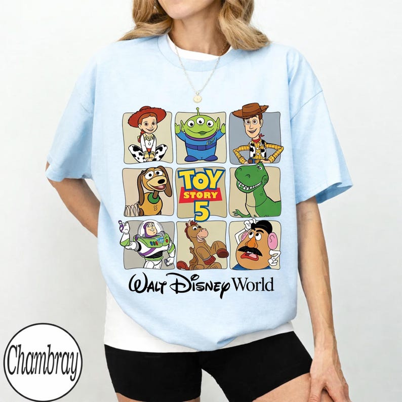 Pode incluir: Camiseta azul claro com uma grade de personagens de Toy Story, incluindo Woody, Buzz Lightyear e Rex. A camisa tamb&eacute;m exibe o texto "Toy Story 5" e "Walt Disney World" em uma fonte divertida. Um design casual e divertido.