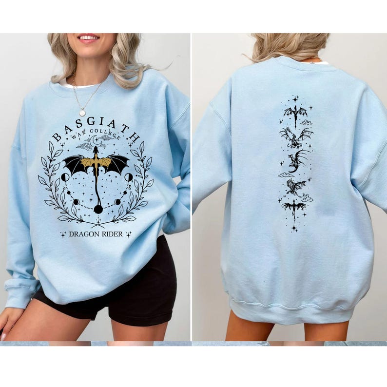 May include: Light blue sweatshirt with a graphic on the front that says "Basgiath War College" with a dragon and umbrella design. The back of the sweatshirt has a vertical design of dragons and other symbols. The sweatshirt is a crew neck.