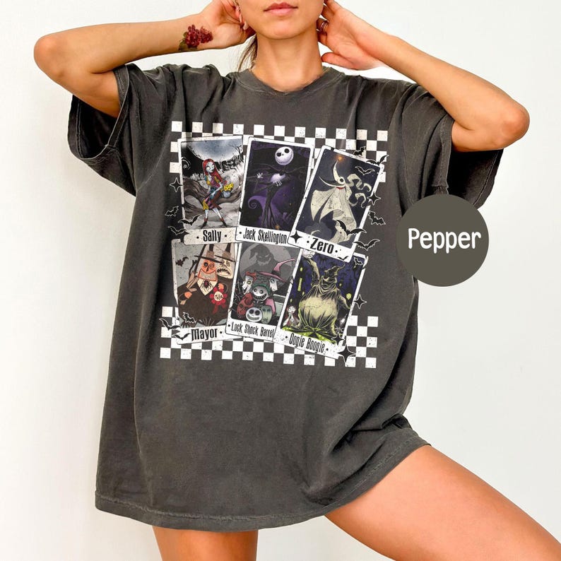 May include: Dark gray t-shirt featuring a graphic of characters from The Nightmare Before Christmas. The design includes images of Sally, Jack Skellington, Zero, the Mayor, Lock, Shock, Barrel, and Oogie Boogie. The shirt has a V-neck.