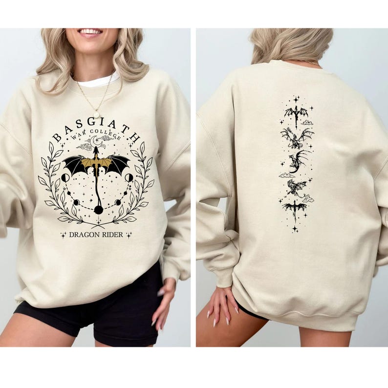 May include: Beige sweatshirt with black graphic design. The front features text that reads "BASGIATH WAR COLLEGE" and "DRAGON RIDER" with a dragon and umbrella design. The back has a vertical arrangement of dragon and sword illustrations.