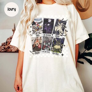 May include: Cream-colored t-shirt featuring six character cards from "The Nightmare Before Christmas." The cards include Sally, Jack Skellington, Zero, Mayor, Lock, Shock, Barrel, and Oogie Boogie. Black bats surround the cards.