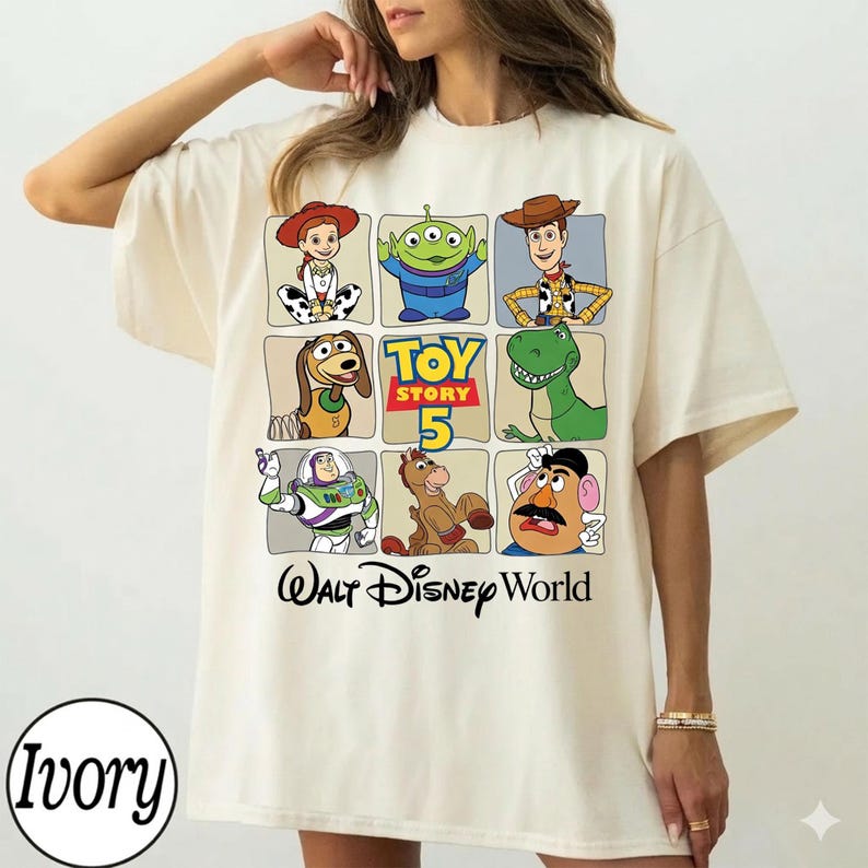 Pode incluir: Camiseta cor marfim com uma grade de personagens de Toy Story, incluindo Woody, Buzz Lightyear e Rex. A camiseta tamb&eacute;m exibe o texto "Toy Story 5" e "Walt Disney World".
