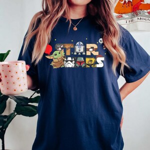 May include: A white ceramic mug with a black handle and the text "But First, Coffee" in a bold, black font. The mug is set against a blurred background, suggesting a cosy setting.