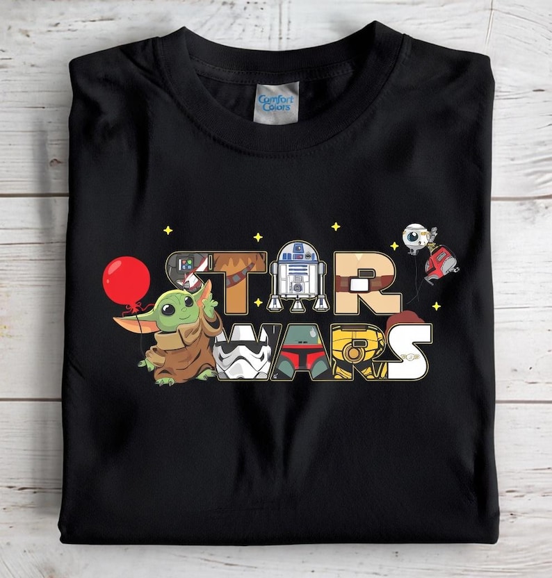 May include: Black t-shirt with a colourful cartoon design of "STAR WARS" and characters like Baby Yoda and R2-D2. The design includes a red balloon held by Baby Yoda and other iconic Star Wars figures.