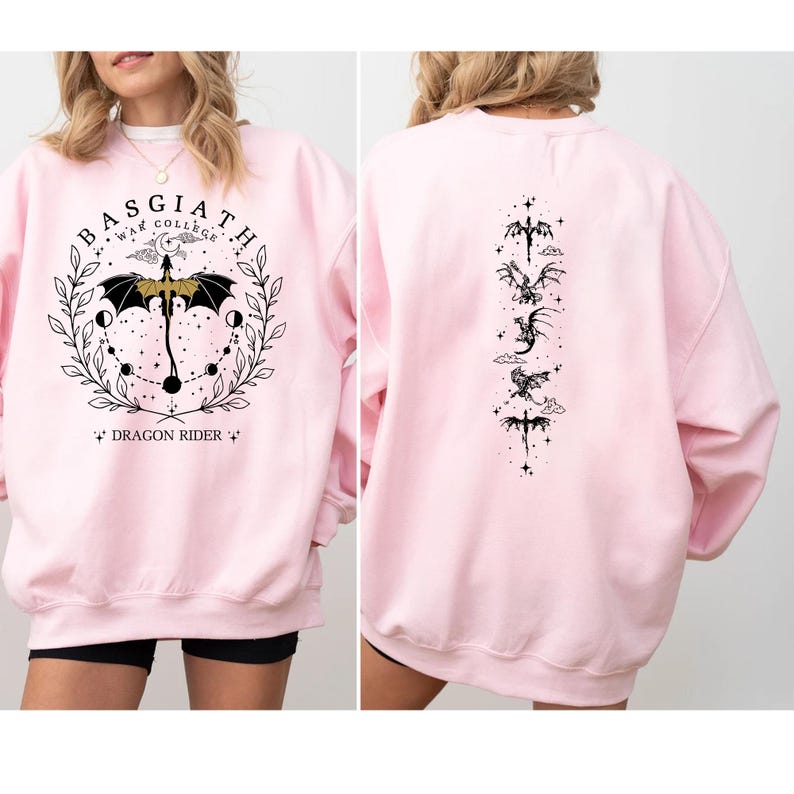 May include: A light pink sweatshirt with a graphic on the front and back. The front features a circular design with the text "BASGIATH WAR COLLEGE" and "DRAGON RIDER". The back has a vertical arrangement of dragon illustrations.