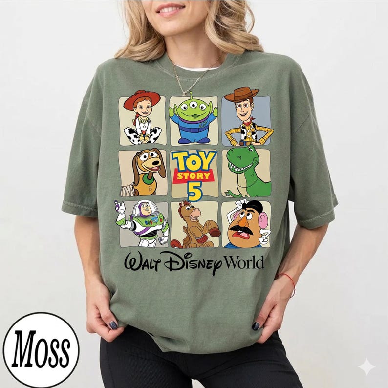 Pode incluir: Camiseta verde-oliva com uma grade de personagens de Toy Story, incluindo Woody, Buzz Lightyear e Rex. A camisa tamb&eacute;m tem o texto "Toy Story 5" e "Walt Disney World" em preto e amarelo.
