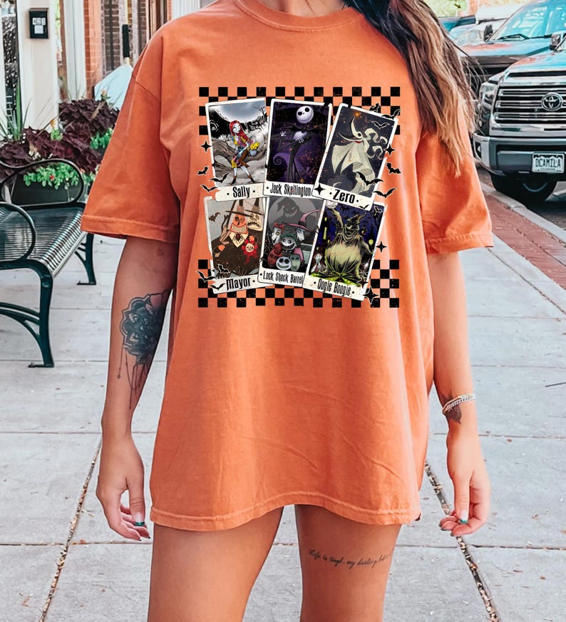 May include: Orange t-shirt featuring a graphic of characters from The Nightmare Before Christmas. The design includes images of Sally, Jack Skellington, Zero, Mayor, Lock, Shock, Barrel, and Oogie Boogie. The design is set against a black and white checkered background.