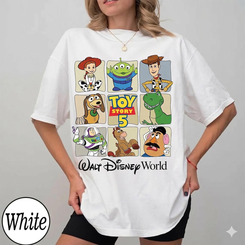 Pode incluir: Camiseta branca com uma grade de personagens de Toy Story, incluindo Woody e Buzz Lightyear. A camiseta tamb&eacute;m tem o texto "Toy Story 5" e "Walt Disney World".