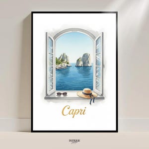 Könnte beinhalten: Gerahmter Kunstdruck mit einer Ansicht von Capri, Italien, durch ein offenes Fenster. Das Bild zeigt einen Strohhut mit blauem Band, Sonnenbrille und das Wort "Capri" in goldener Schrift. Die Szene zeigt das Meer und zwei große Felsformationen.