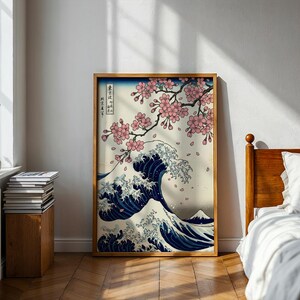 Könnte beinhalten: Ein gerahmter Druck eines japanischen Holzschnittkunstwerks. Das Kunstwerk zeigt eine große Meereswelle in Blau- und Weißtönen, mit Kirschblüten und einem Berg im Hintergrund. Der Rahmen hat eine hellbraune Farbe.
