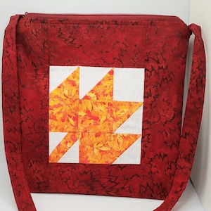 May include: A red quilted tote bag with a zipper closure and a long strap. The bag features a patchwork design with a white and orange star in the center.
