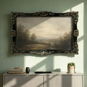 Puede incluir: Una pintura de paisaje enmarcada en un marco ornamentado cuelga de una pared verde claro. La pintura representa una escena natural con árboles, un río y un cielo nublado. El marco es oscuro con detalles decorativos. Un mueble debajo contiene libros, una figura de búho y un mando a distancia.