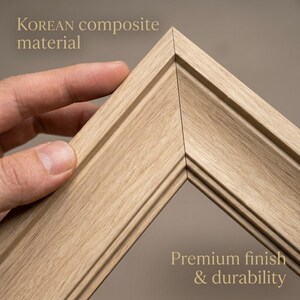 Puede incluir: Primer plano de una esquina de un marco de fotos de madera marrón claro. El marco está hecho de material compuesto coreano y tiene un acabado de primera calidad para mayor durabilidad. El texto "KOREAN composite material" y "Premium finish & durability" son visibles.