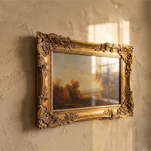 Puede incluir: Pintura de paisaje enmarcada en un marco dorado ornamentado. La escena representa un paisaje sereno con árboles y agua. El marco presenta diseños florales y de volutas detallados.