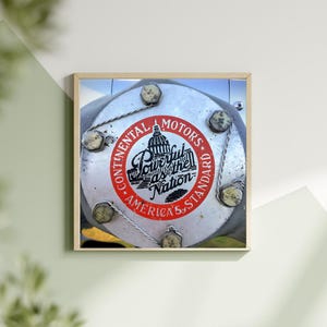 May include: A close-up of a silver engine part with a red and white sticker that reads "Continental Motors Powerful as the Nation America's Standard". The sticker features a black and white illustration of the Capitol Building.
