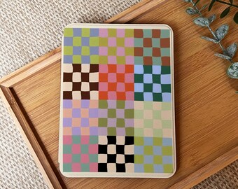 May include: A rectangular coaster with a colorful checkerboard pattern. The design features squares in shades of brown, orange, green, blue, pink, and purple. The coaster is set on a wooden tray, suggesting a home decor item.