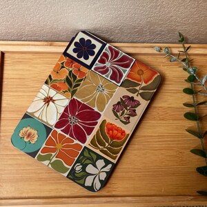 Puede incluir: Una bandeja decorativa rectangular con un estampado floral. La bandeja presenta una cuadr&iacute;cula de dise&ntilde;os florales coloridos en tonos naranja, rojo, blanco y verde. La bandeja est&aacute; colocada sobre una superficie de madera.