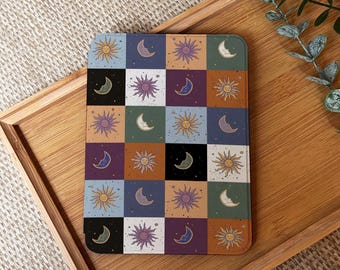 May include: A square tablet case with a celestial theme, showcasing a patchwork design of suns and crescent moons in various colours. The squares alternate between light blue, orange, green, purple, and black, creating a visually appealing pattern.