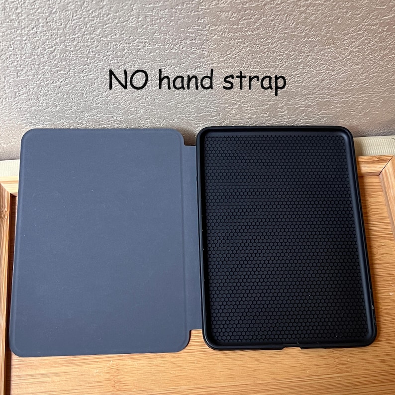 Puede incluir: Una funda de tableta gris abierta con un interior negro. La funda est&aacute; sobre una superficie de madera. El texto "NO hand strap" est&aacute; encima de la funda.