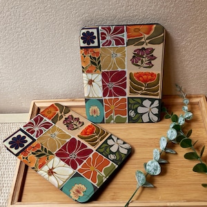 Puede incluir: Dos estuches con un dise&ntilde;o floral de patchwork, uno rectangular y otro cuadrado, est&aacute;n colocados sobre una bandeja de madera. Los estuches presentan una variedad de flores en rojo, naranja, amarillo y blanco, sobre un fondo beige. El estuche cuadrado est&aacute; inclinado hacia el espectador.