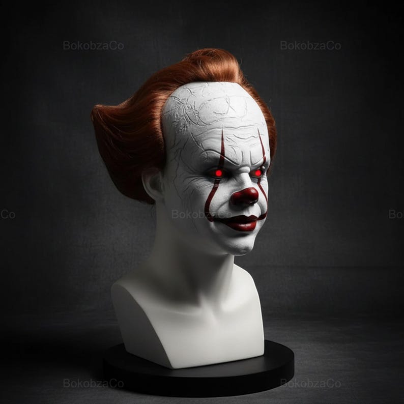 May include: A white bust of a clown with red hair, a red nose, and red eyes. The clown has white face paint with red accents around the mouth and eyes. The bust is on a black base.