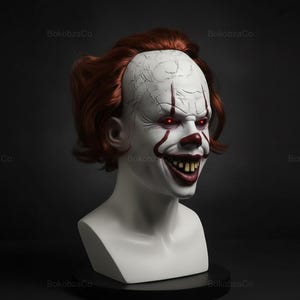 May include: A white clown mask with red hair, red nose, and red accents around the mouth and eyes. The mask has a sinister grin with yellow teeth and glowing red eyes. The mask is displayed on a white bust against a dark background.