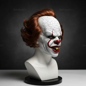 May include: A white bust of a scary clown with red hair, a red nose, and a sinister grin. The clown's face is painted white with red accents around the mouth and eyes. The bust is on a black base.