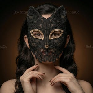 以下が含まれることがあります： 黒いレースの猫マスク。目の周りに金色のラインストーンのアクセント。マスクの上部には猫の耳の形があり、複雑な花のレース模様があります。目と鼻を覆い、神秘的でエレガントな外観を作り出しています。