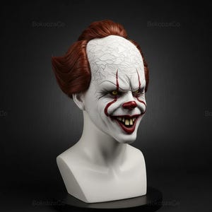 May include: A white bust of a clown with red hair, a white face, and a sinister grin. The clown has red accents around the mouth and eyes, with yellow eyes and visible teeth. The bust is on a black surface.