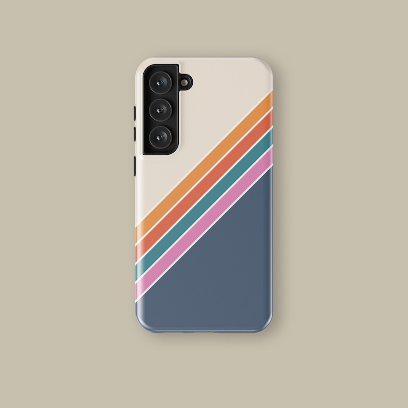 May include: A smartphone case with a retro design. The case features a cream-coloured top section and a navy blue bottom section, divided diagonally. The design includes orange, teal, and pink stripes. The phone has a triple-lens camera.