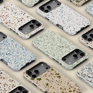 Può includere: Diverse custodie per telefoni con un motivo a terrazzo in vari colori, tra cui bianco, blu, verde e beige. Le custodie hanno una finitura lucida e un ritaglio nero per la fotocamera. Le custodie sono disposte a griglia.