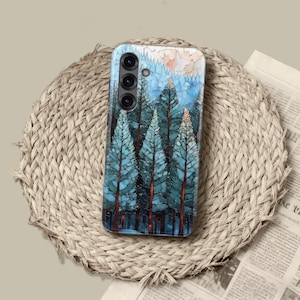 Può includere: Una custodia per smartphone con una scena di foresta con alberi alti color verde acqua e cielo blu. Gli alberi hanno tronchi marrone-rossastro. La custodia è su un sottobicchiere circolare intrecciato.